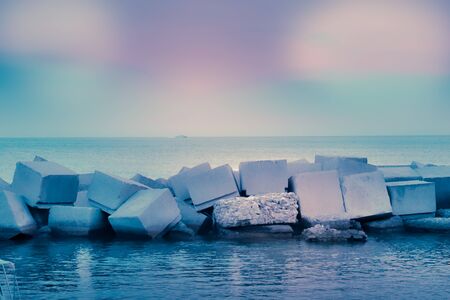 Square stone breakwaters in calm turquoise water with reflection and pink fairy sky sea horizon lines. Salerno, Italyの写真素材