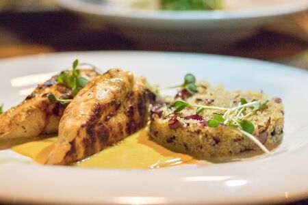 Cous cous and grilled chicken fillet with sause and cress salad served on white plate in restaurantの写真素材