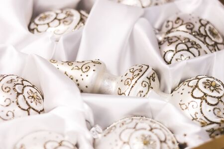Delicate christmas tree toys pearly balls and top painted with a golden glitter ornaments on a white silk cloth. Soft focus background cardの写真素材