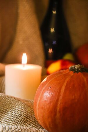 Happy Thanksgiving post card. Autumn holidays still life. Home warmth orange pumpkin close up with white soft warm candle light, fruits and bokeh in stars shape on wine bottle on sackcloth background.の写真素材