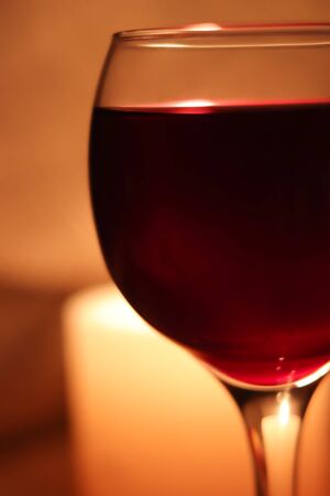Blurred soft focus bokeh of glass full of red wine glowing from candle light winery background.の写真素材