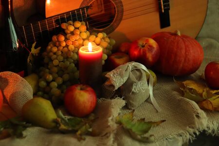 Autumn warm scene. Stll life harvest. Thanksgiving post card greetings. Candle flame with ripe fruits and bottle of wineの写真素材