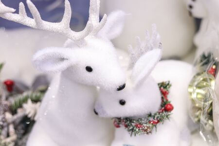 Christmas and new year winter holidays decoration. Snow-white beautiful sweet figures of mother deer with white fur and sparkling horns sitting with her baby in tinsel necklaceの写真素材