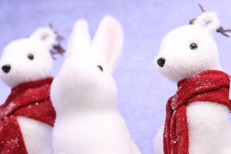 Christmas winter holidays home party decoration cute white toys fluffy furry white animals rabbit and minks in red scarfs in snow on a blue backgroundの写真素材