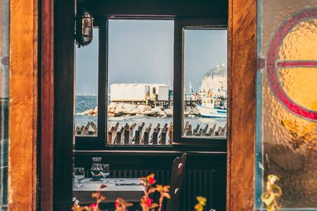 Sorrento, Marina grande seascape sea view framed through the window of small beach restaurant with table and glasses. Amalfi coast, authentic italian fishmen village in Campania, Italy.の写真素材