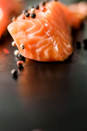 Raw sea red salmon fish fillet uncooked piece with colorful peppercorns on black background.の写真素材
