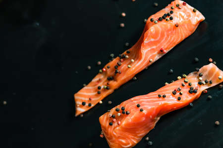 Raw sea red salmon fish fillet two uncooked pieces with colorful peppercorns on black background.の写真素材