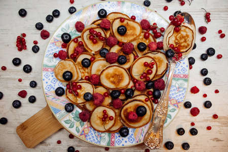 Mini pancakes with scattered berries on patterned plate and silver spoon in rustic style....