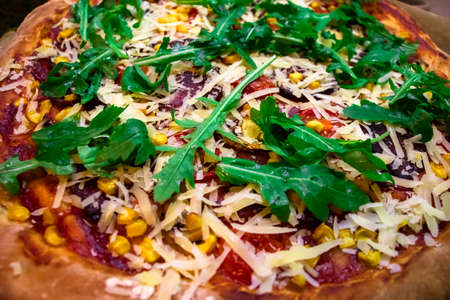 Pizza with fresh green arugula, parmesan cheese, salami, sweet corn, mushrooms and cherry tomatoes food background. Freshly baked homemade pizza.の写真素材
