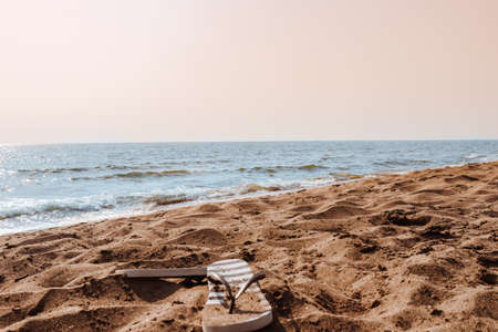 Summer beach at the sea with stripped flip-flops on sand on sunny day with blue water and pink clear sky. Italy, vacation at Tyrrhenian sea.の写真素材