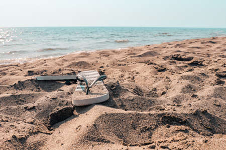 Summer beach at the sea with flip-flops on a brown sand on sunny day with blue water and clear sky. Italy, vacation at Tyrrhenian sea.の写真素材