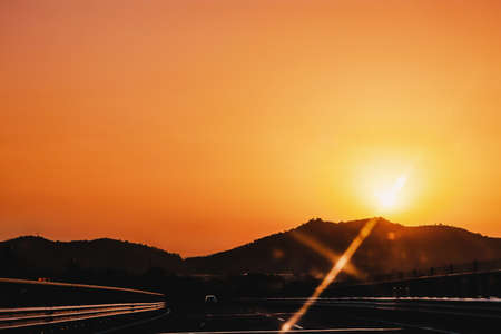 Scenic view of orange sky picturesque sunset and highway with single car driving on it on a way to mountains silhouette. Beautiful Summer dusk landscape of monti Lattari near Naples, Campania, Italyの写真素材