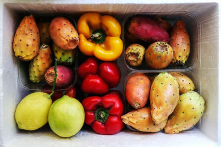 Colorful fresh and raw fruits and vegetables: prickly pears, opuntia cactus figs, raw yellow and red pepper bells and lemons in white box at street market top view photo. Frutta e verdura Italiana.の写真素材