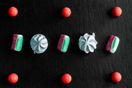 Sweets colorful candies, marmalade and marshmallow organized pattern top view on a black slate stone board with space for text.の写真素材