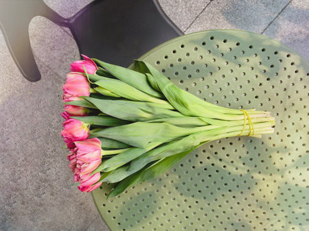 Bouquet of blooming pink tulips with leaves laying on green cafe table. Top view photo with space for text. Beautiful Spring flowers present. flower shop concept.の写真素材
