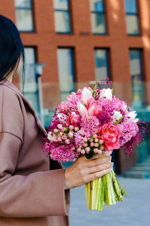 Beautiful, brunette Ukrainian young woman in cozy autumn clothes drinking cappuccino and smiling sitting outdoors in center of city Kyiv city with fall season pumpkin flower composition on tableの写真素材