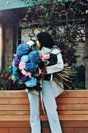 Beautiful, brunette Ukrainian young woman in cozy autumn clothes drinking cappuccino and smiling sitting outdoors in center of city Kyiv city with fall season pumpkin flower composition on tableの写真素材