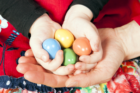 Little girl holding Easter eggs in her and motherâs hands. Colorful background.の写真素材