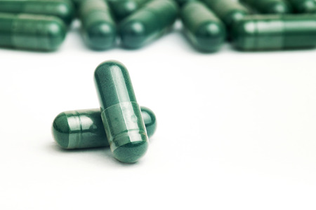 Selective focus of spirulina capsule with Brown herbal leaf isolated on white backgroundの写真素材