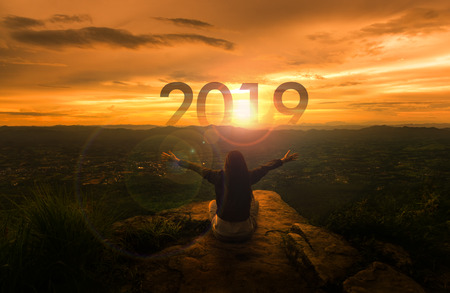 Happy New year 2019 concept : Yong sitting over the cliff and raise the hand up on sunset timeの写真素材