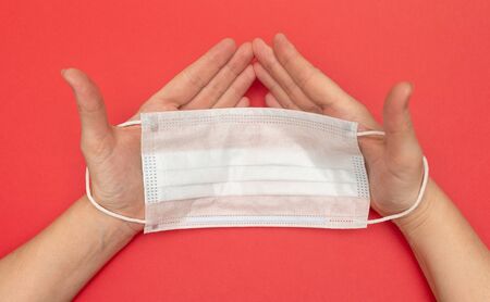 medical mask protection against virus and disease in hands closeup on a red background, at home on...