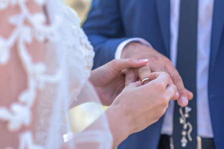 the bride in a white lace dress puts a ring on the groom's hand.の写真素材