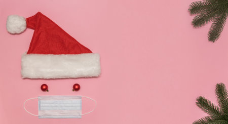 santa claus hat instead of eyes balls instead of a mouth a mask protecting from the virus. spruce branches in the corners green for designの写真素材