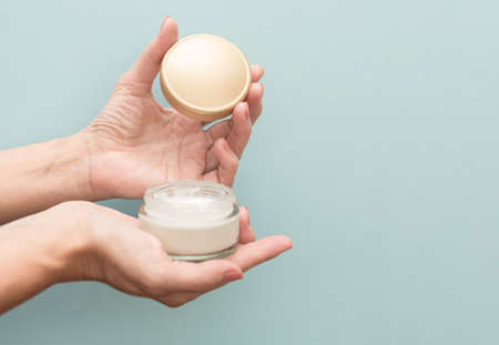 In female hands a jar with a lid of white cream on a blue background. For moisturizing and caring for the skin.の写真素材