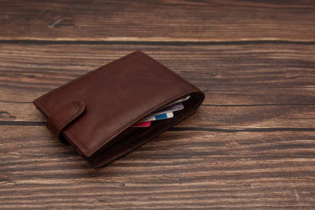 Closed mens brown wallet on a wooden brown background with business cards