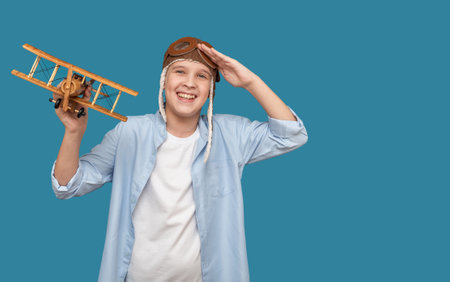 A child on a blue background in a pilot's hat and with an airplane toy. Rejoices and smiles. On a blue background.の写真素材