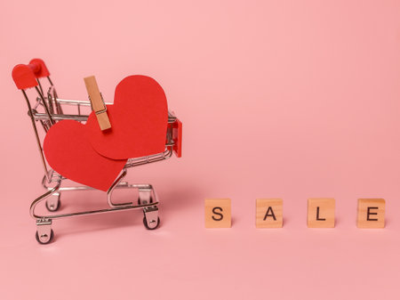 Mini shopping cart from the supermarket. Valentine's Day. Discount word made from wooden letters. On a pink background.の写真素材