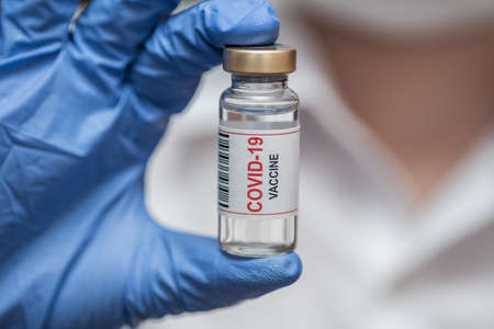 Vaccine in ampoule. From the coronavirus. The doctor keeps in blue gloves. Close-up.の写真素材