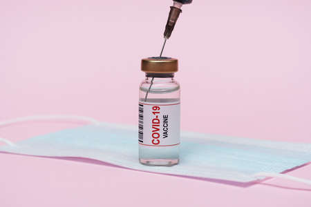 COVID-19 vaccine ampoule, protective mask. Vial with a vaccine against the virus. On a pink background.の写真素材