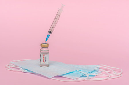 Vaccine ampoule, protective mask. Vial with a vaccine against the virus. Pink background.の写真素材
