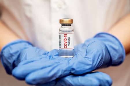 Vaccine in ampoule. From the coronavirus. The doctor keeps in blue gloves. The finger points to the vaccine.の写真素材