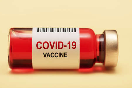 Ampoule of COVID-19 vaccine isolated on yellow background. Vial with red vaccine against the virus....