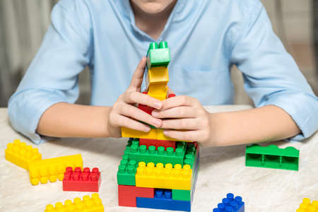 The boy plays at home on the table with plastic cubes. Close-up.の写真素材