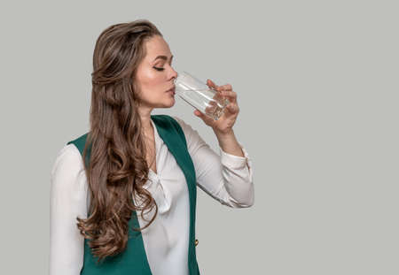 young beautiful woman in a green jacket brunette with long hair drinks water from a glass