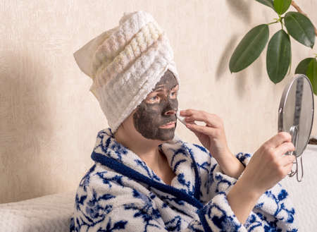 Old woman makes a black cosmetic mask on her face at home.の写真素材