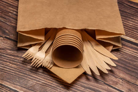 The craft package contains disposable tableware, forks, knives and glasses. On a wooden brown background.の写真素材