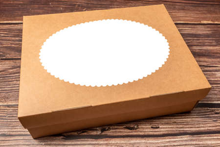 Brown paper box on wooden background. Design cutout on the box lid. Gift wrapping box.の写真素材