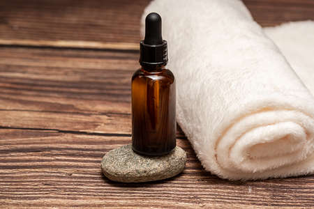 Cosmetic oil stands on a stone. There is a white towel next to it. On a wooden background.の写真素材