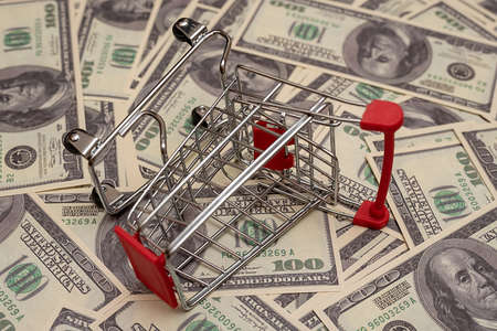 A small cart from a supermarket lies sideways against a background of dollars.の写真素材