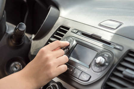 The hand in the car turns the volume button. The dashboard in the car. Close-up.