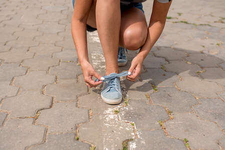 A woman is sitting and tying her shoelaces in the summer on the street. Close-up.の写真素材