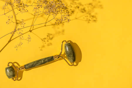 Jade green roller with dry flowers. On a yellow background. Facial care.