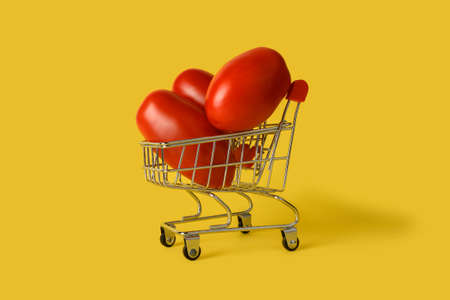 Mini shopping basket with tomatoes isolated on yellow background. Retail. Online sales concept.の写真素材