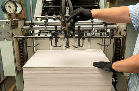 Old large format printing press. Womans hands are holding paper.