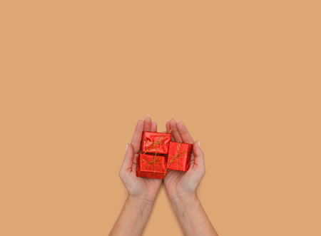 Hands hold a gift box made of red paper. On a beige background.の写真素材