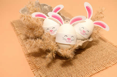 Children's crafts for Easter from eggs. Bunnies with ears in a box. On burst. On a beige background.の写真素材